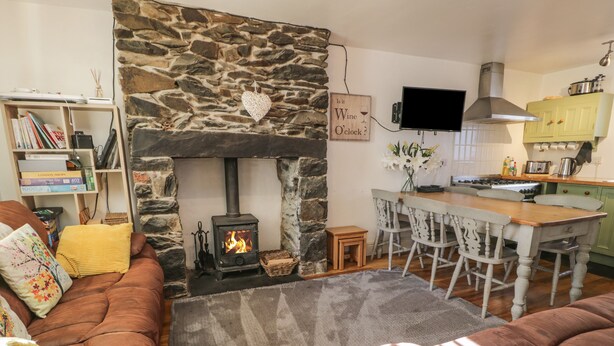 Ein gemütliches Wohnzimmer mit Kamin aus Stein, einem darüber angebrachten Fernseher und einem Essbereich mit Holztisch und Stühlen.