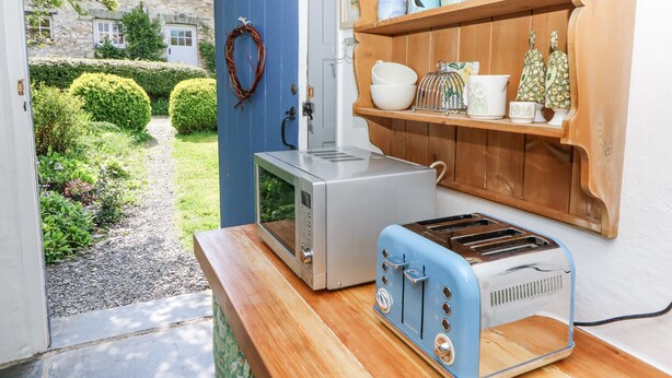 A kitchen with a microwave, toaster, and wooden shelves with dishes. - Hawthorn Cottage (Llandysul)