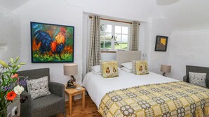 A bedroom with a large bed, a chair, a nightstand, a lamp, and a painting on the wall. - Hawthorn Cottage (Llandysul)