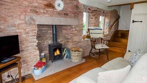 A cozy living room with a brick fireplace, a television on a wooden stand, and a white sofa. - Rose Cottage (Monmouth)