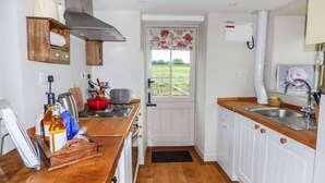 A compact kitchen with wooden countertops, a built-in stove, and a window with a view of the outdoors. - Rose Cottage (Monmouth)