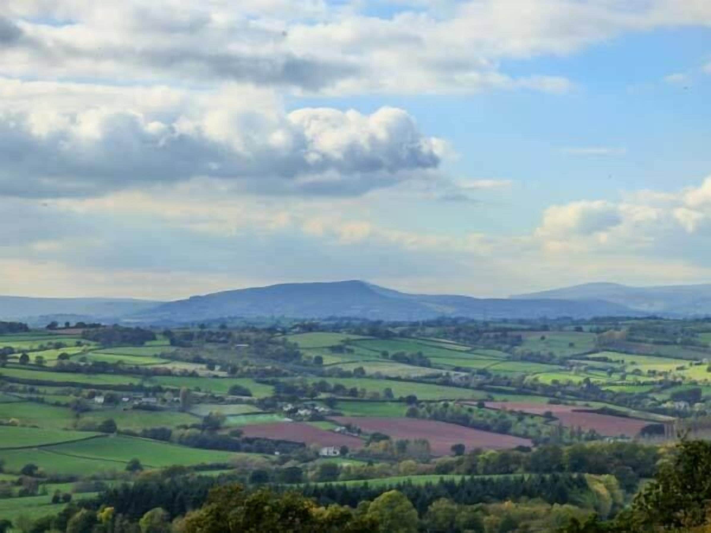 A panoramic view of rolling green fields, a distant mountain, and a partly cloudy sky.