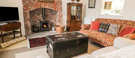 A cozy living room with a brick fireplace, a television, a sofa with patterned cushions, and a wooden cabinet.