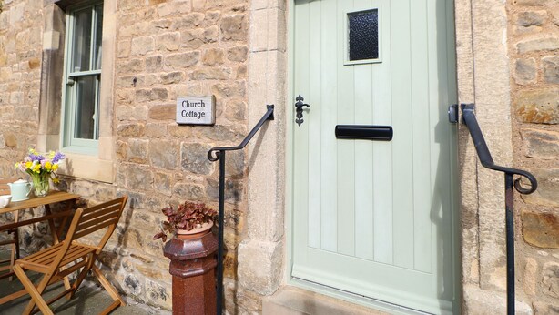 A stone building with a green door, a sign reading "Church Cottage," and a small window.