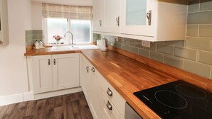 A kitchen with white cabinets, a wooden countertop, a black induction cooktop, and a window with a frosted glass pane.