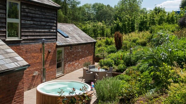 Une maison en bois avec une partie en briques, un jacuzzi et une terrasse avec des meubles d’extérieur.