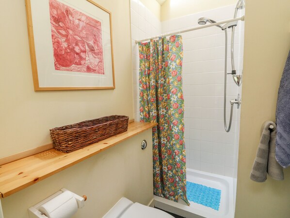 A bathroom with a shower, a toilet, a sink, a framed picture on the wall, and a basket on a shelf.