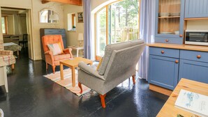 A cozy living room with a wooden ceiling, a dining area with a table and chairs, and a kitchen with blue cabinets and a microwave. - The Garden Flat (Fort William)