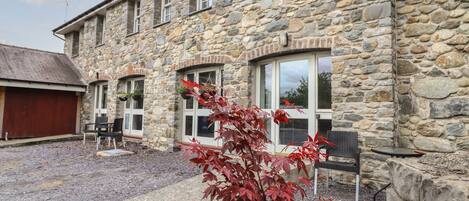 A stone building with a garage, a patio with chairs, and a red-leafed plant in the foreground.