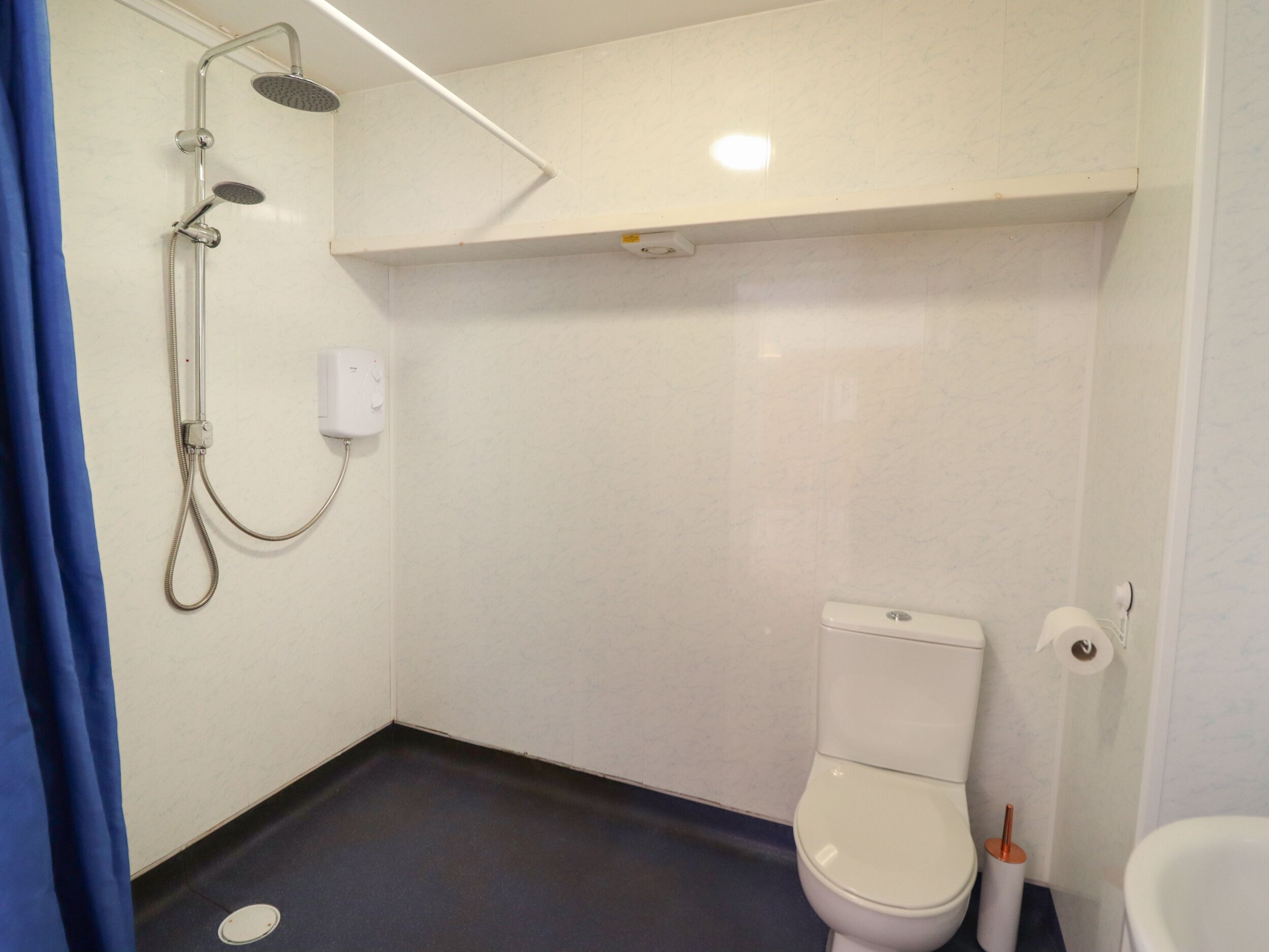 Ein kleines, modernes Badezimmer mit Toilette, Dusche und einem blauen Duschvorhang.
