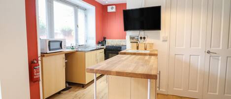 Cocina compacta con armarios de madera, microondas, estufa y televisor de pantalla plana sobre la encimera.