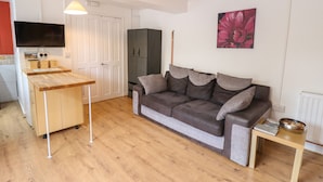 Ett kompakt bostadsutrymme med ett litet kök, en soffa, ett matbord och en TV.