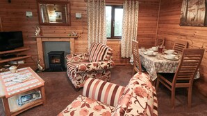 A cozy cabin interior with wooden walls, a fireplace, a sofa, a dining table with chairs, and a television. - Sycamore Lodge (Saltburn-by-the-Sea)