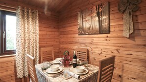 A wooden cabin interior with a dining table set for four, a window with curtains, and a forest-themed wall decoration. - Sycamore Lodge (Saltburn-by-the-Sea)