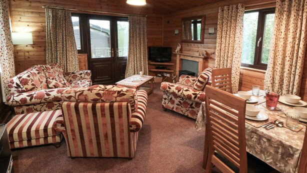 A cozy cabin interior with wooden walls, a sofa set, a dining table with chairs, and a fireplace. - Sycamore Lodge (Saltburn-by-the-Sea)
