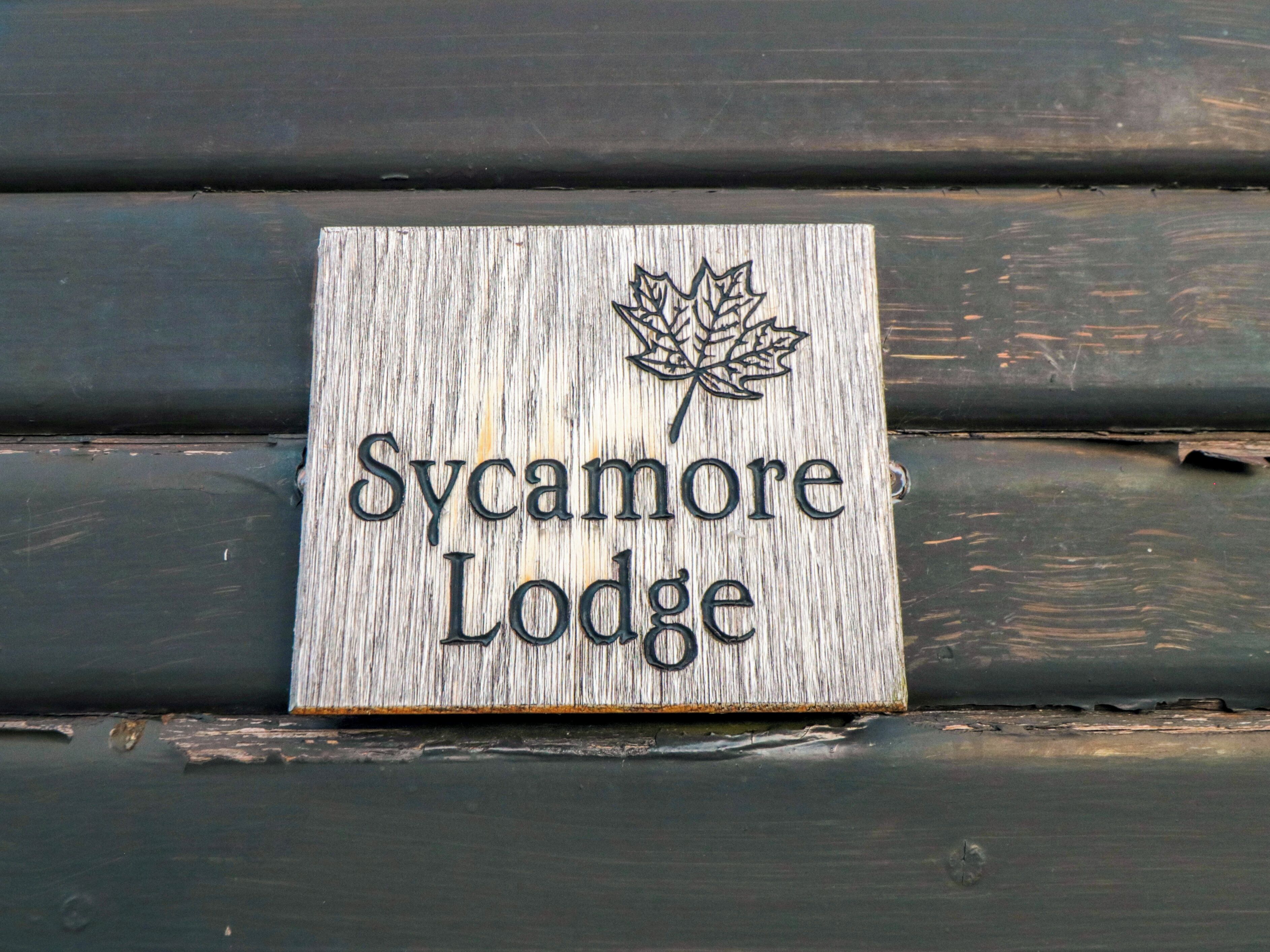 A wooden sign with the text "Sycamore Lodge" and a maple leaf design.