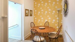 Un comedor con una mesa redonda y cuatro sillas, una pared con diseño de lunares amarillos, y una lámpara de pie.