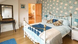 Un dormitorio con cama, mesita de noche, cómoda, espejo y puerta que da a otra habitación.