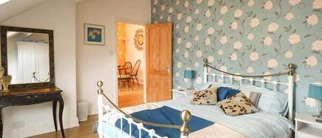 A bedroom with a bed, a nightstand, a dresser, a mirror, and a door leading to another room.