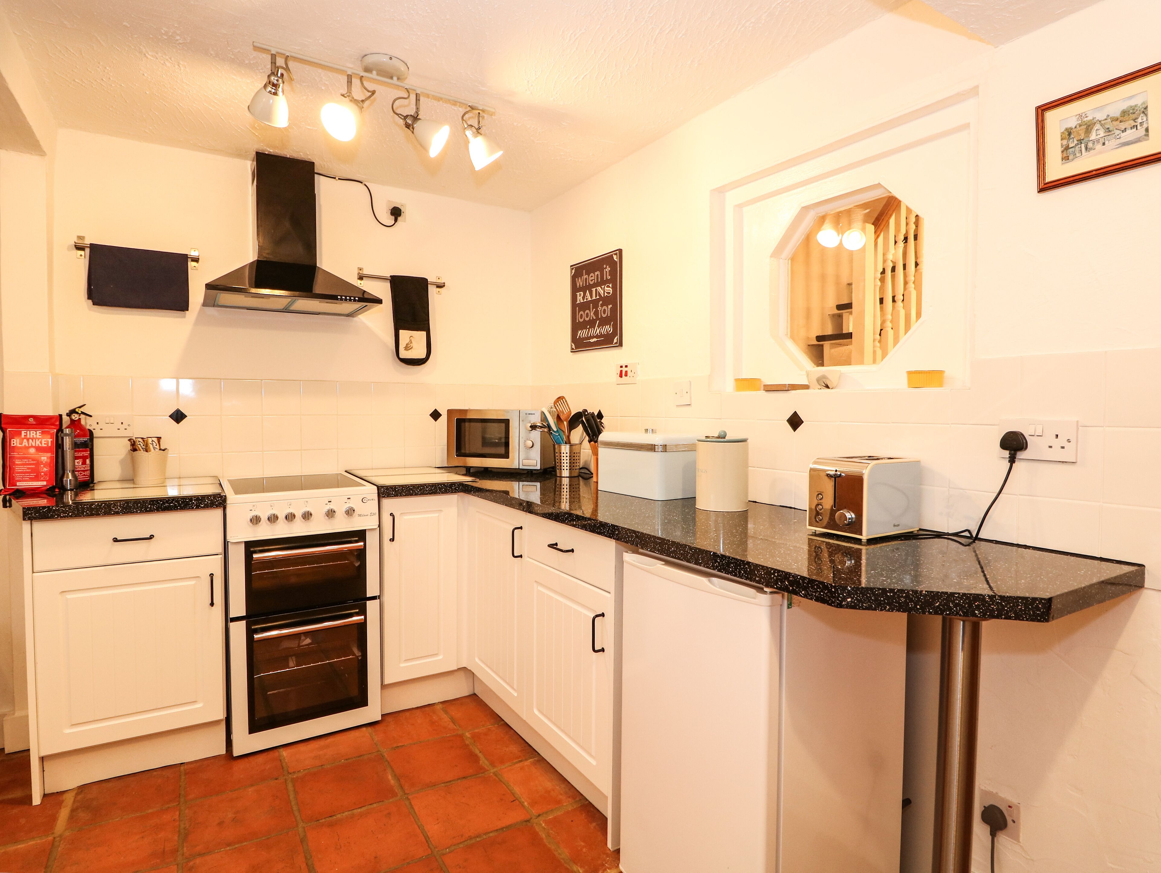 A kitchen with white cabinets, a stove, an oven, a microwave, and a toaster. There is a fire blanket on the counter, and a sign on the wall.