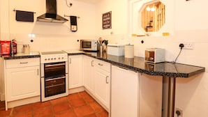 A kitchen with white cabinets, a stove, an oven, a microwave, and a toaster. There is a fire blanket on the counter, and a sign on the wall. - Duck Cottage (King's Lynn)