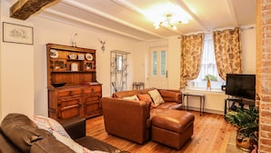 A living room with a brown leather sofa, a wooden cabinet, a television, and a window with curtains. - Duck Cottage (King's Lynn)