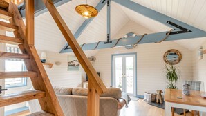 Ein geräumiges Zimmer mit einer Holztreppe, einem Sofa, einem Esstisch und einer Pendelleuchte.