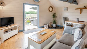 Ein gemütliches Wohnzimmer mit Fernseher, Couch und Couchtisch aus Holz. Ein Balkon mit Geländer und einer Pflanze ist ebenfalls vorhanden.