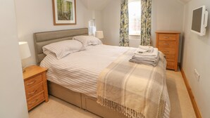 Une chambre à coucher comprenant un lit, des tables de chevet, une commode, un tableau, une fenêtre avec des rideaux et un téléviseur fixé au mur.