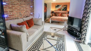 A modern living room with a brick wall, a sofa, a TV, and a patterned rug. - Smithy Cottage (Cemaes Bay)