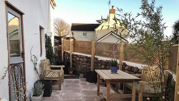 Een terras met een stenen vloer, houten meubels en planten in potten.