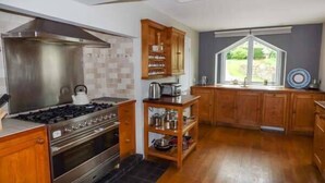 Een moderne keuken met houten kasten, een gasfornuis en een groot raam met uitzicht op de omgeving.
