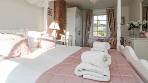 Een slaapkamer met een groot bed, een dressoir, een nachtkastje, een lamp en een raam met gordijnen.