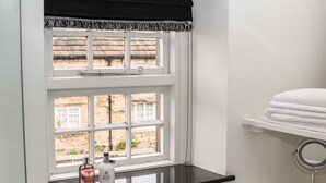 A bathroom with a window, a shelf with toiletries, and a towel rack. - Ash Cottage (Bakewell)