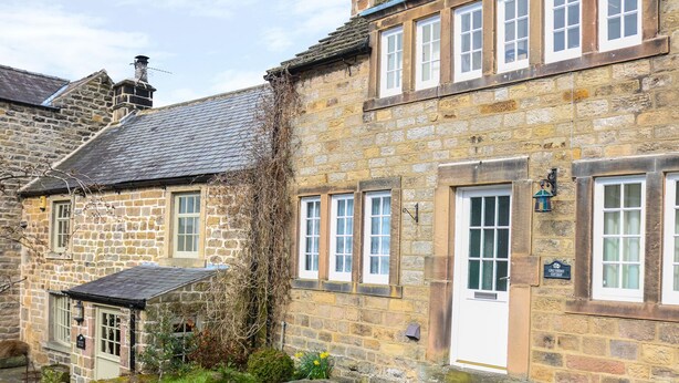 A stone cottage with a white door, a small garden, and a stone wall. - Ash Cottage (Bakewell)