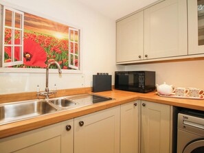 A kitchen with a stainless steel sink, a microwave, and a washing machine. - Swallows Cottage (Shrewsbury)
