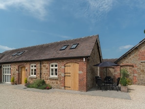 A stone building with a tiled roof, wooden doors, and a patio area with outdoor seating. - Swallows Cottage (Shrewsbury)