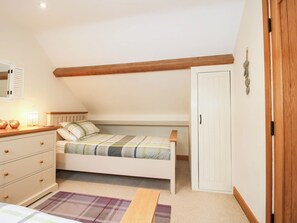 A bedroom with a bed, a dresser, a nightstand, a lamp, and a door. - Swallows Cottage (Shrewsbury)