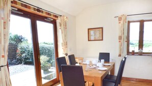 Un coin repas avec une table en bois et des chaises noires, de grandes fenêtres avec des rideaux et un tableau encadré au mur.