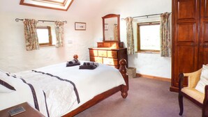 Une chambre à coucher avec un grand lit, une commode en bois et une armoire. Il y a des fenêtres avec des rideaux et une lucarne.