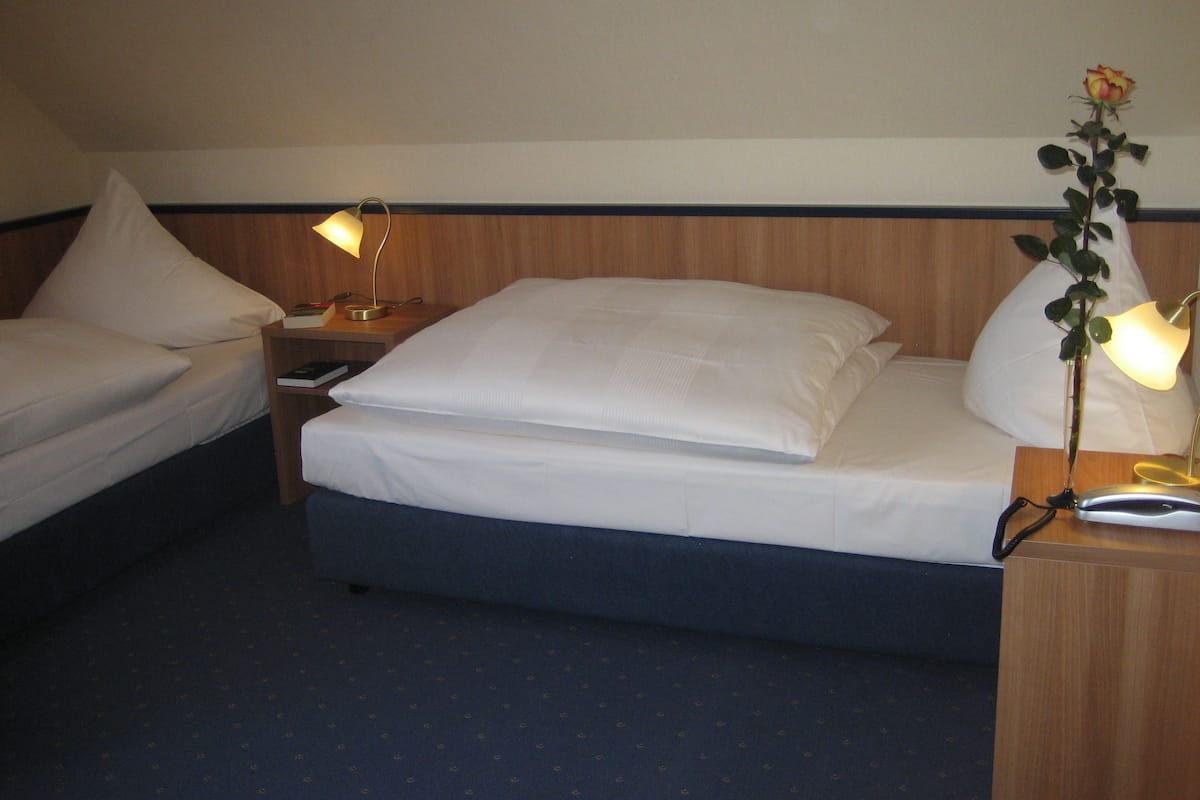 A hotel room with two single beds, a wooden headboard, bedside lamps, a bedside plant, and a small table with a lamp.