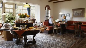 Un rincón comedor acogedor con una mesa de madera, un banco y un tapete estampado. Dos personas están sentadas en una mesa con un jarrón de flores.