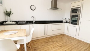 A modern kitchen with white cabinets, a black countertop, a stainless steel range hood, and a double oven. - Marina View (Whitby)