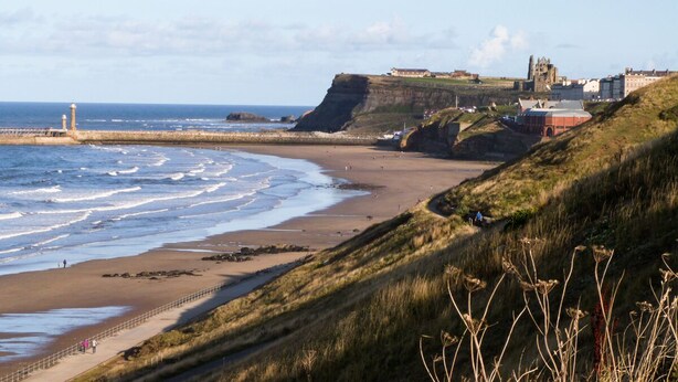 A coastal landscape with a beach, cliffs, and a historic building. - Marina View (Whitby)