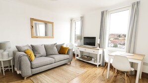 A modern living room with a grey sofa, a wooden coffee table, a TV, and a dining area with a white table and chairs. - Marina View (Whitby)