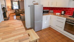 A modern kitchen with white cabinets, a stainless steel refrigerator, a wooden dining table, and a red-tiled backsplash. - Tryfan (Caernarfon)