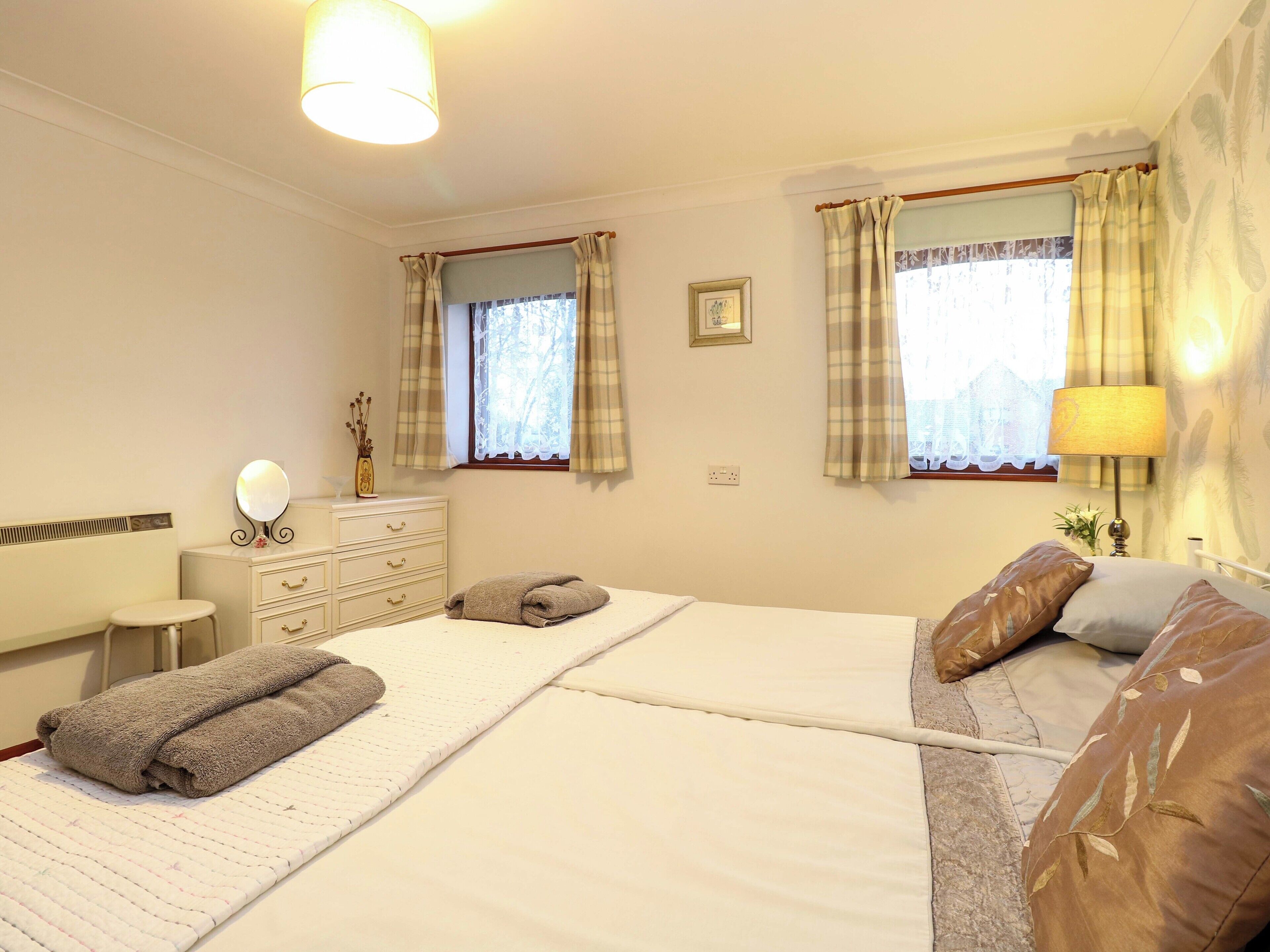 A bedroom with two beds, a dresser, a mirror, and a window with curtains.