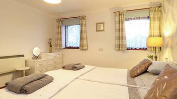 A bedroom with two beds, a dresser, a mirror, and a window with curtains.