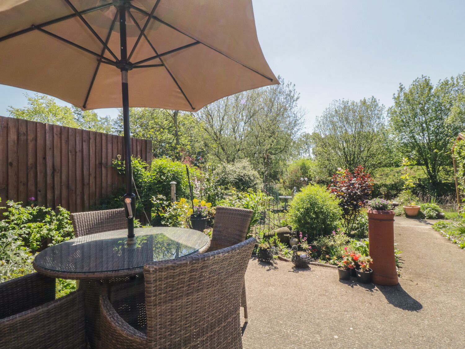 An outdoor patio with wicker furniture, a glass table, and a large umbrella.