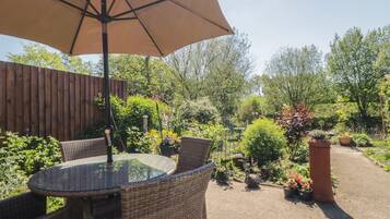 An outdoor patio with wicker furniture, a glass table, and a large umbrella.
